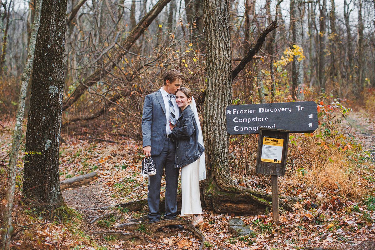 A couple standing together beside a Frazier Discovery Trail signpost in late autumn woods