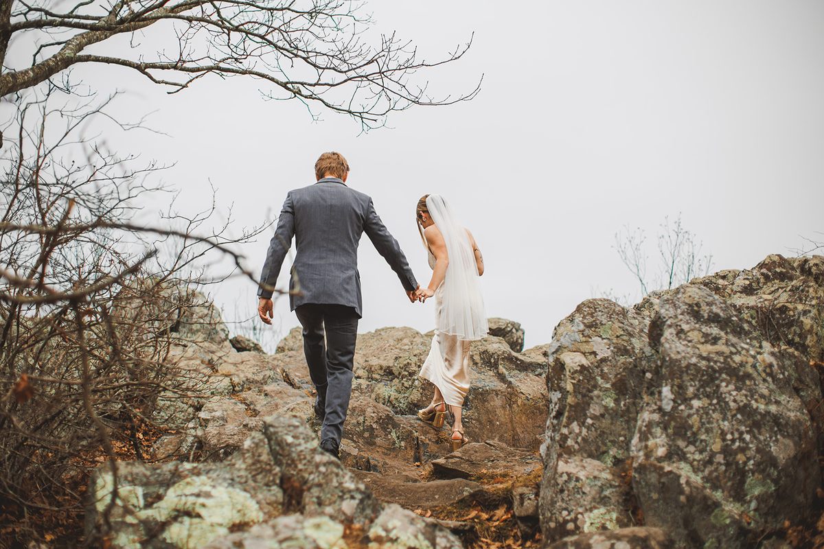A couple picking their way hand in hand across a boulder field on a bare winter ridge