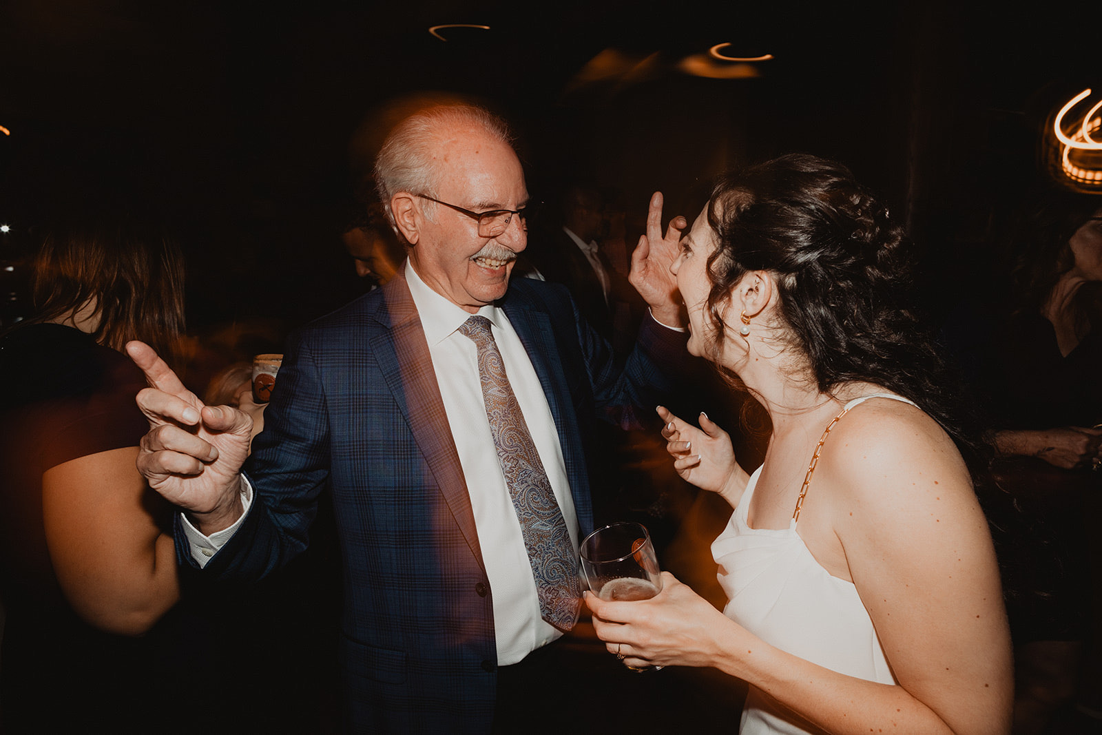 An older guest laughing face to face with the bride at a dark reception