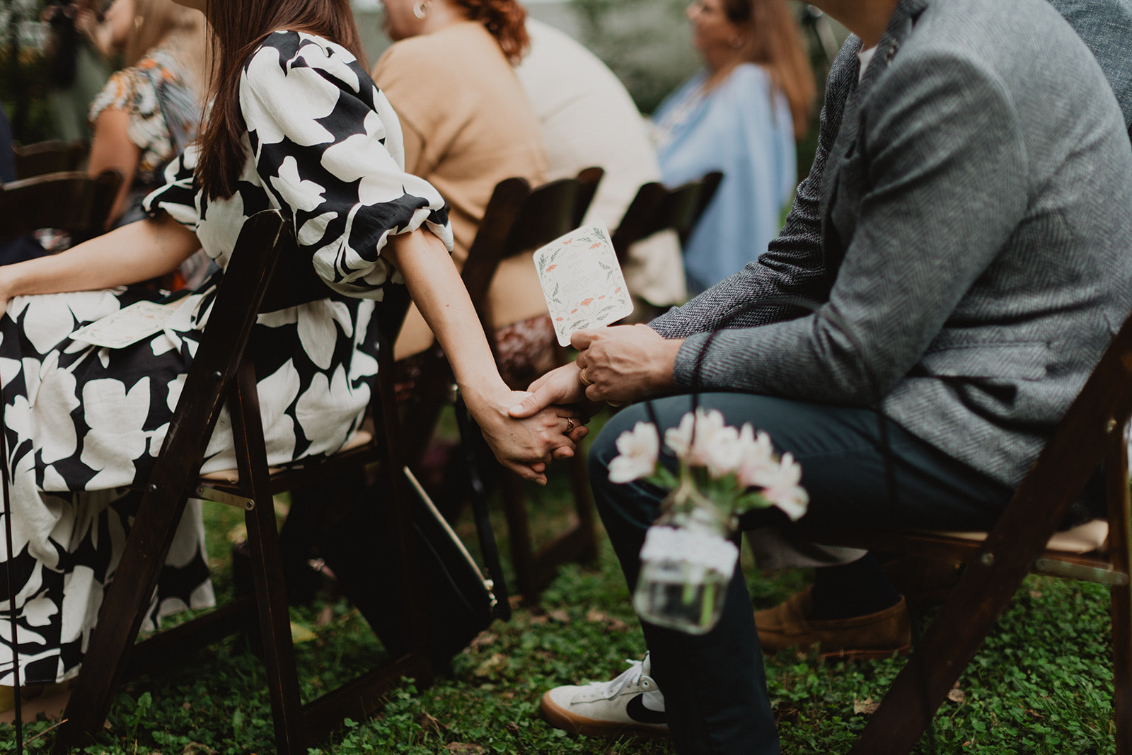 Two seated ceremony guests holding hands across their chairs
