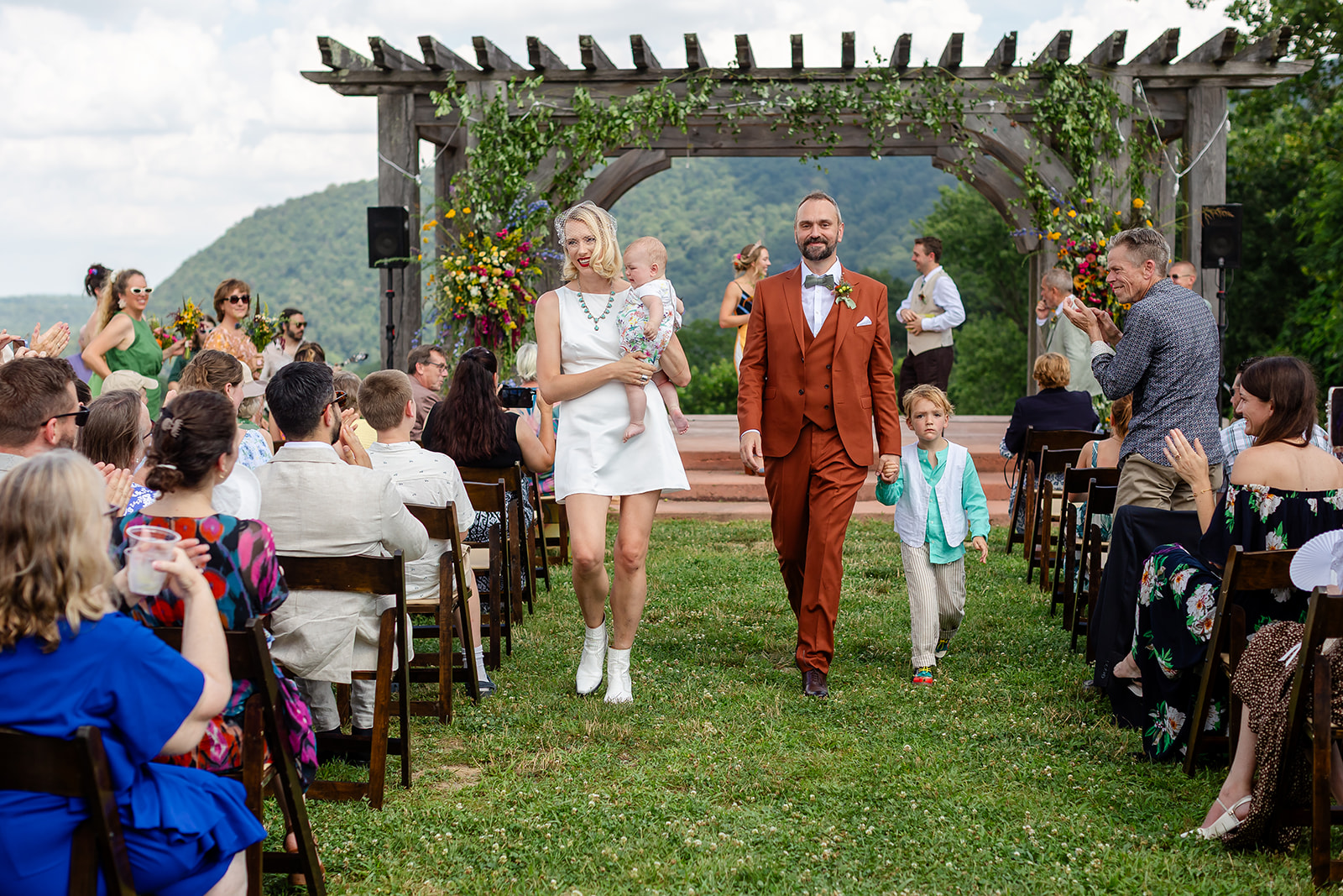 A family walking down the aisle to applause with mountains behind the pergola