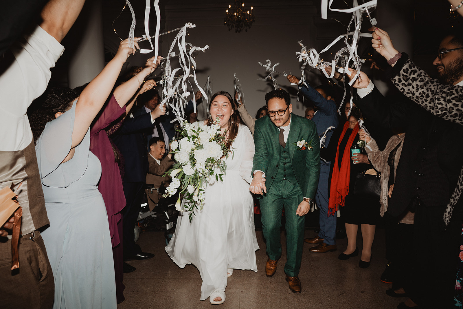 A ribbon-wand exit with the bride laughing and guests cheering on both sides