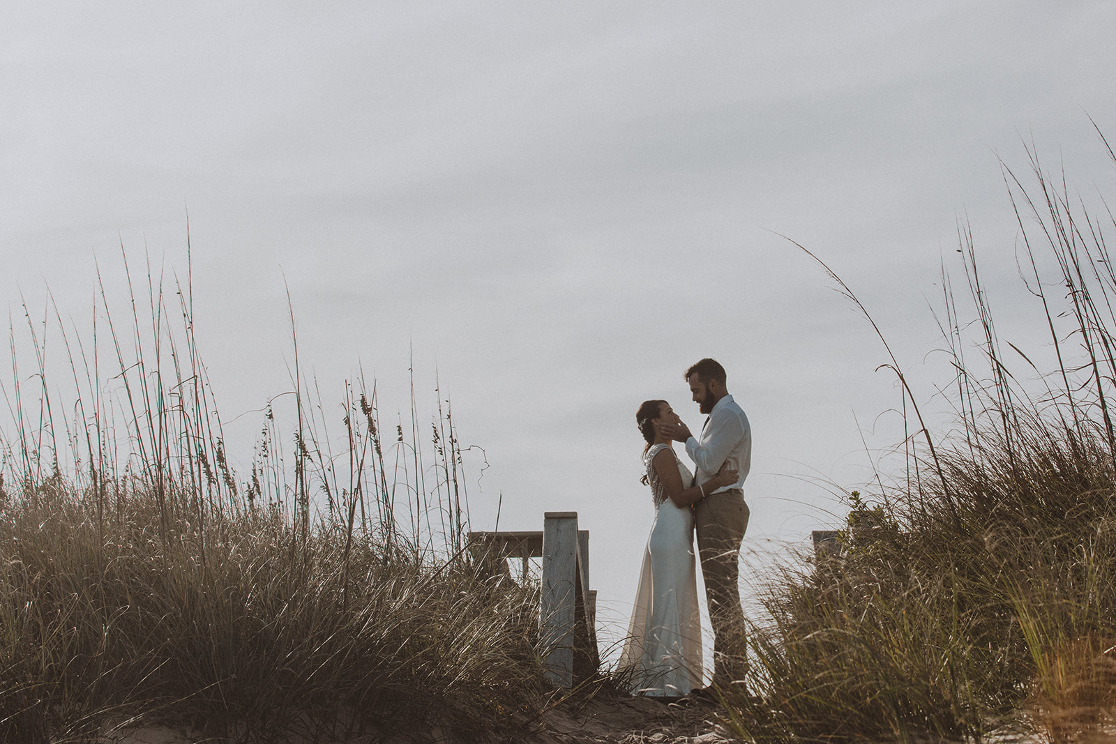 Bride and groom standing together in the dune grass near the beach