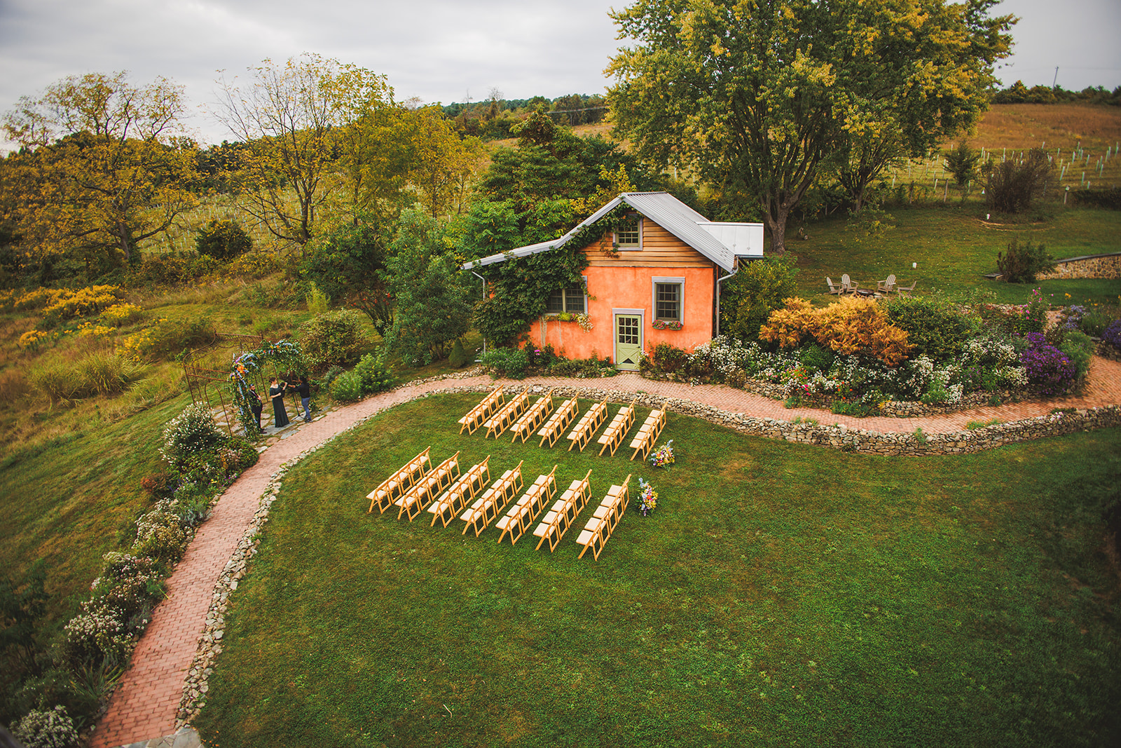 The orange cottage at Zigbone Farm Retreat from above, a brick path curving past garden beds to ceremony chairs on the lawn