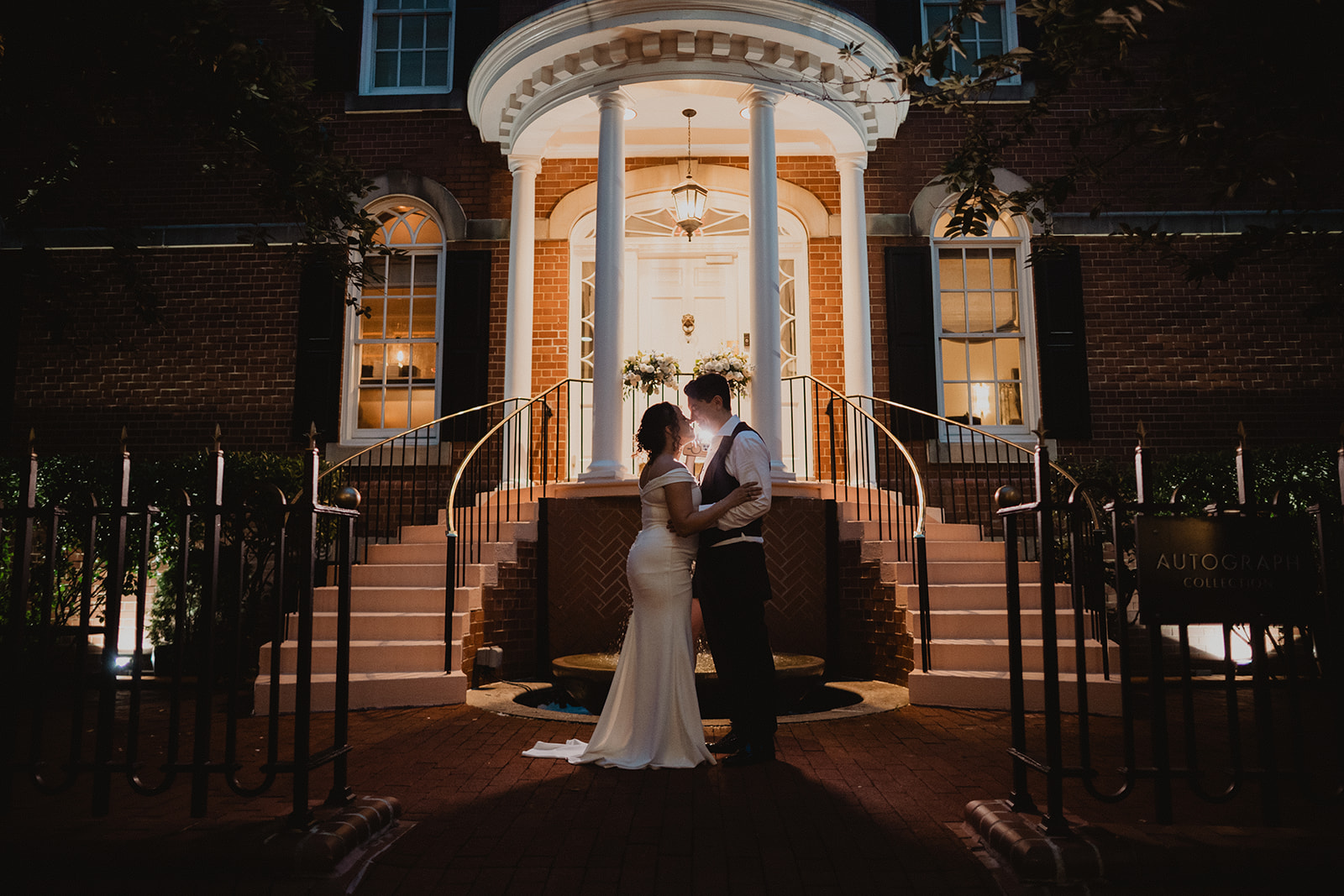 Jessica and Nicholas at night beneath the lantern-lit portico of the Morrison House, curved iron railings sweeping down on both sides