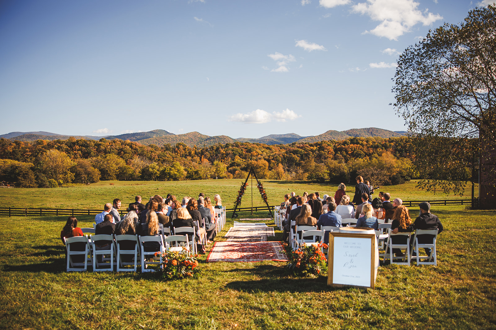Sara and Ryan's ceremony at River's Bend Ranch: a triangle arch and rug-lined aisle facing the autumn Blue Ridge under a blue sky