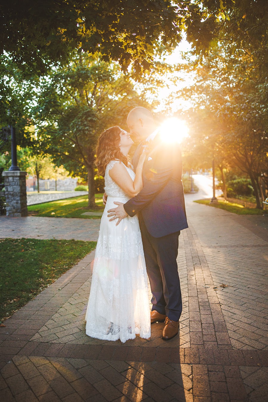 Alex and Phil nose to nose on a brick path at golden hour, the sun bursting between them through the trees