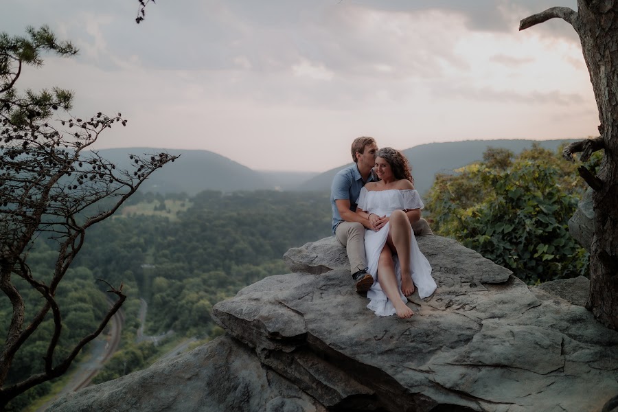Ashley and Alan seated on the boulder at Weaverton Cliffs, pines framing the hazy ridgelines below