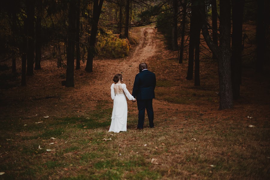 Delaney and Dante walking hand in hand toward a path through dark pines, rust-colored needles underfoot