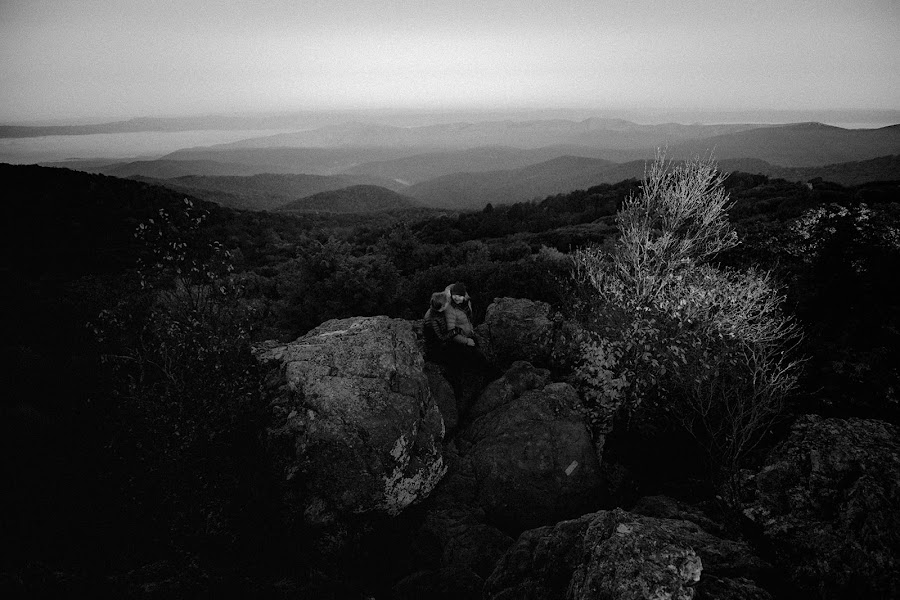 Black and white frame of Lilly and Arthur small among the summit boulders, layered ridges fading to the horizon