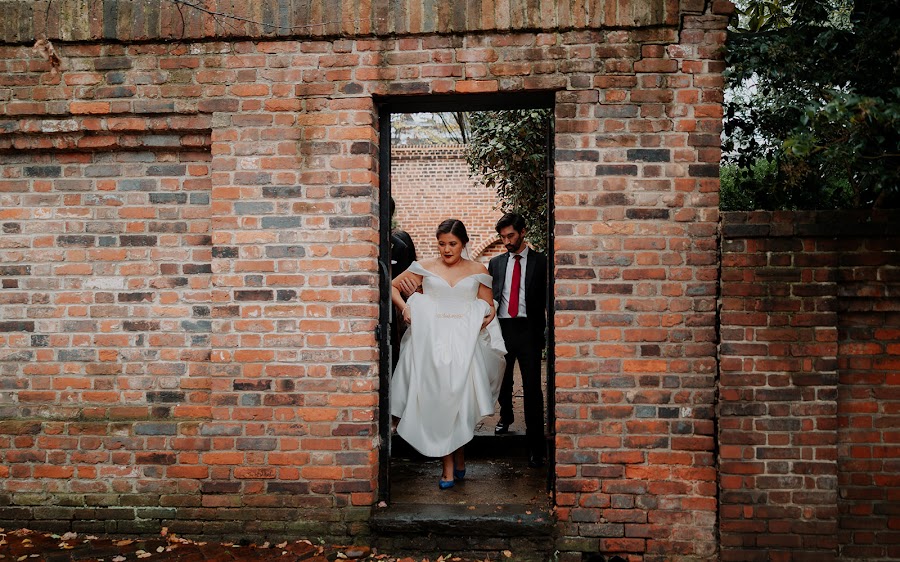 Marrissa lifting her dress as she steps through a doorway in the weathered brick garden wall at The Athenaeum