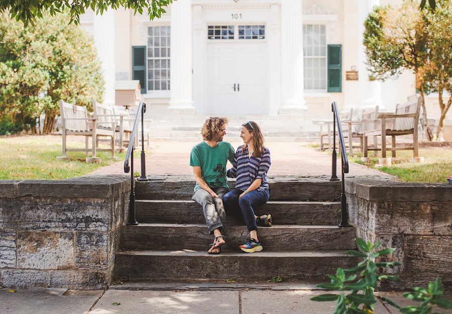 Meredith and John seated on wide stone steps between iron handrails, tall white double doors and green shutters behind them