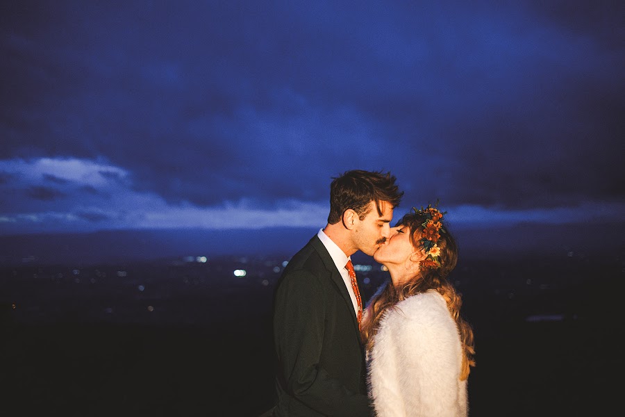 Sara and Ryan kissing at blue hour, her flower crown catching the last light and the valley towns glowing far below