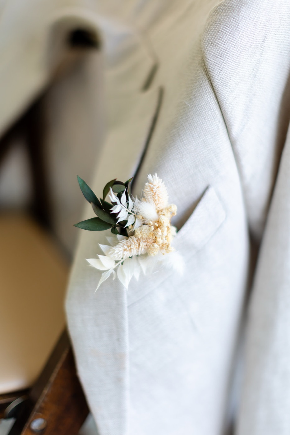 A dried-floral boutonniere of bunny tails, preserved eucalyptus and white botanicals pinned to a natural linen lapel