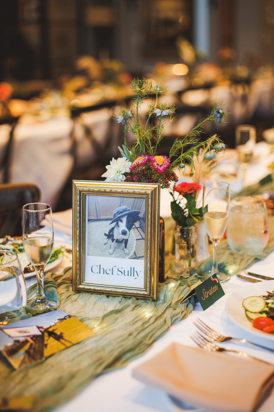 A gold-framed reception table sign reading Chef Sully with a photo of the couple's dog in a hat, on a candlelit table