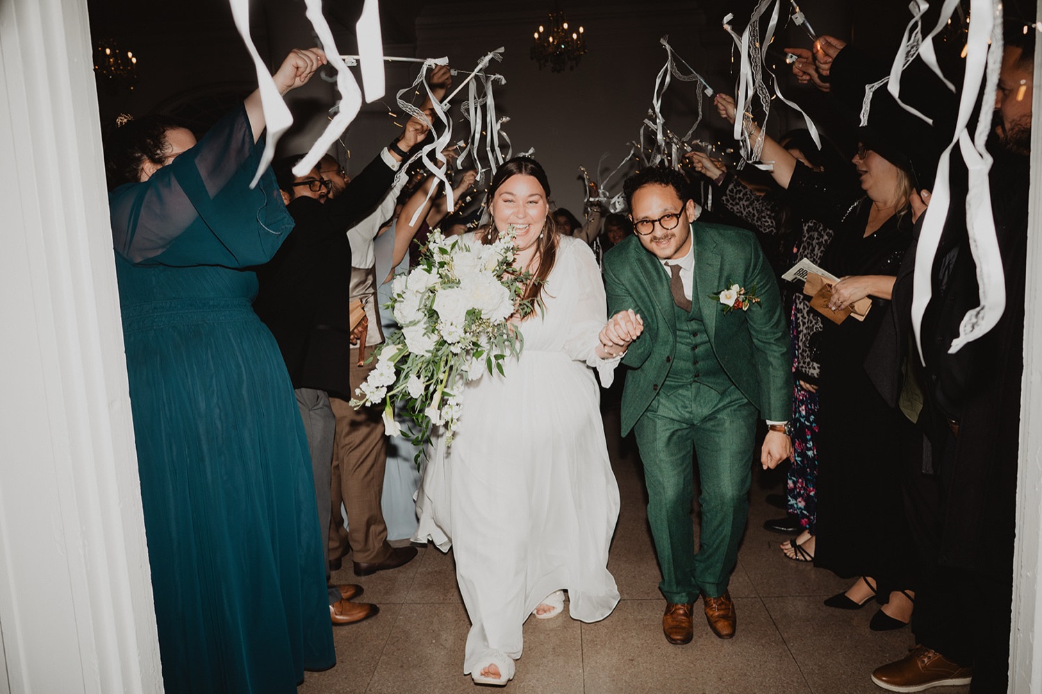 A couple beaming as they walk out through a tunnel of guests waving white streamers